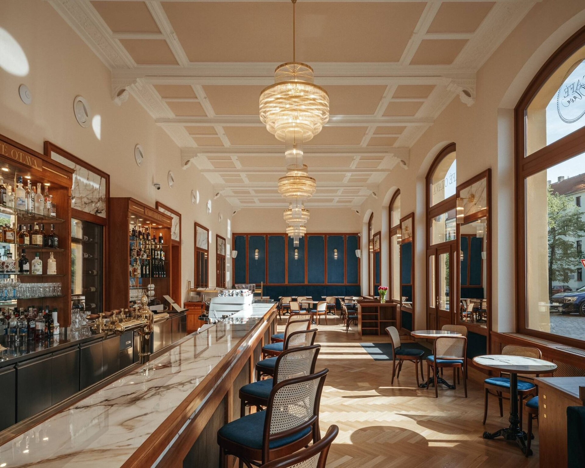 Eingangsbar des Café Otava mit Marmorplatte, hölzernem Tresen und drei Messingleuchtern unter der Kassettendecke
