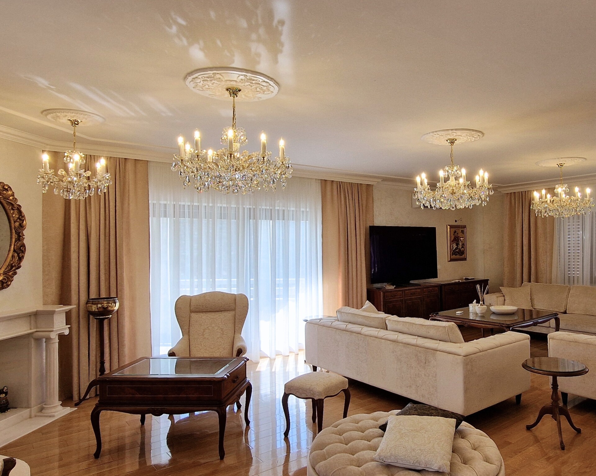 Wohnzimmer mit Kristall-Kronleuchtern, cremefarbenen Sofas und Kamin
